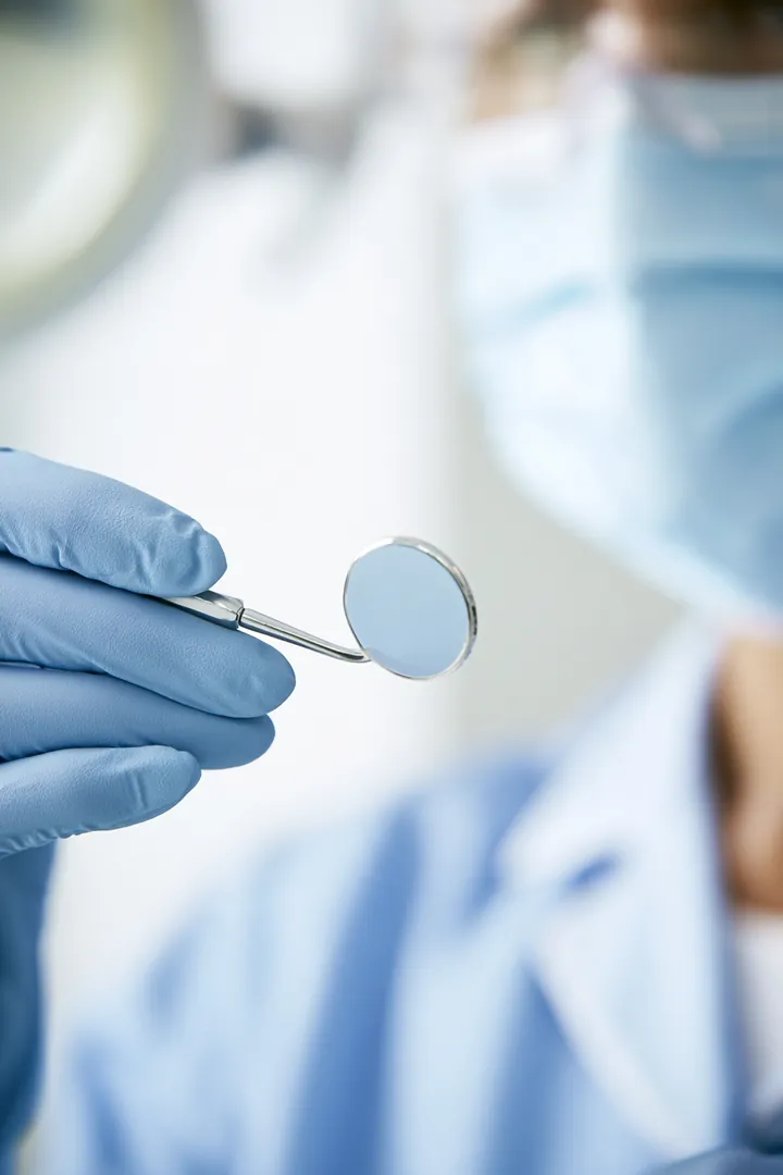 Dental hygienist's gloved hands holding a dental mirror in a bright modern dental office