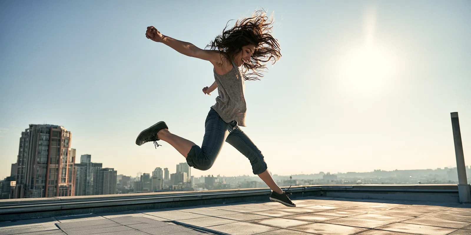 Woman in her 20s leaping in celebration on a sunny city rooftop terrace after finishing an avant lending payoff plan
